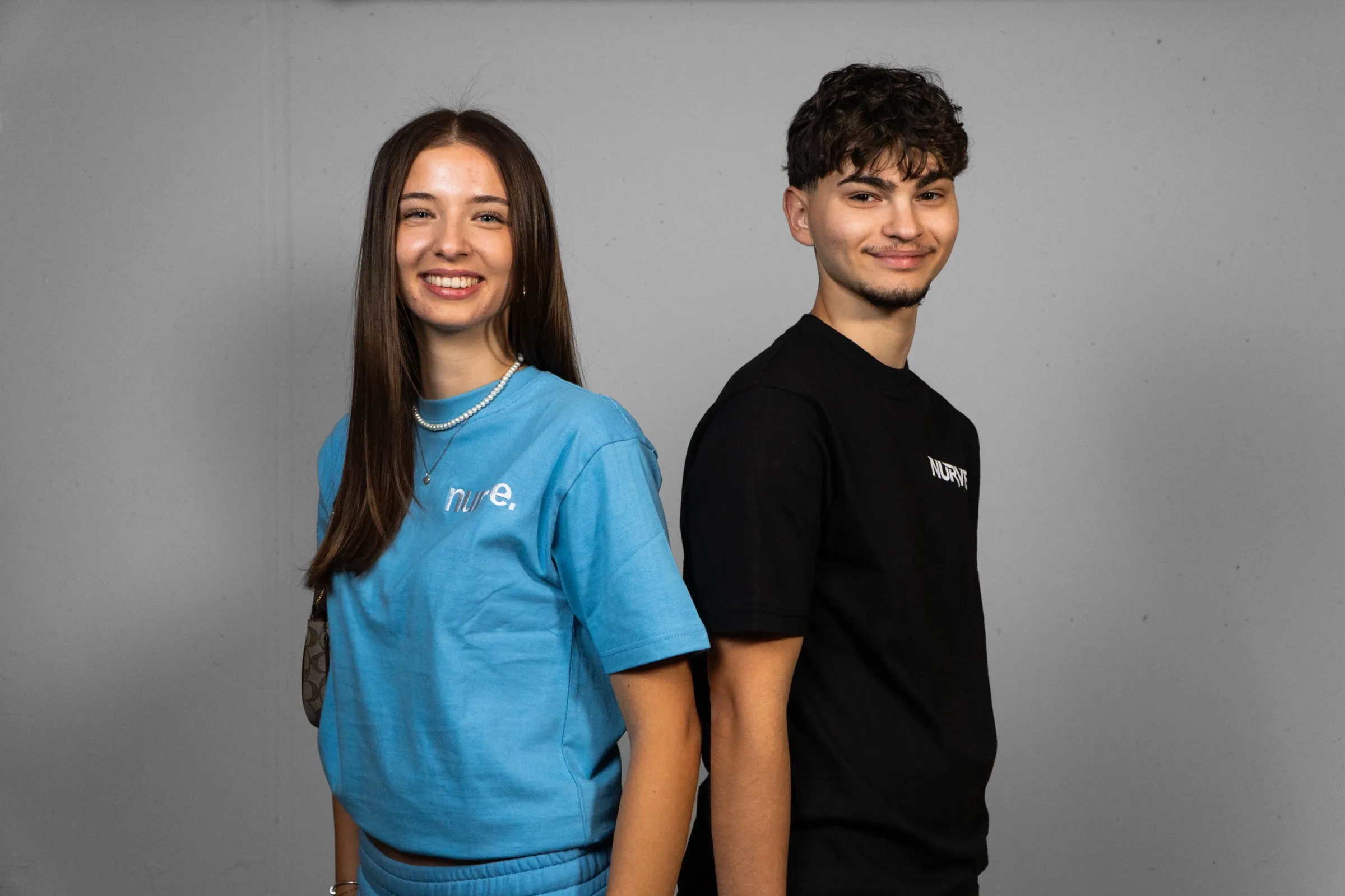 Zwei Models in Shirts der Marke NURVE, eine Frau in Hellblau und ein Mann in Schwarz, vor grauem Hintergrund